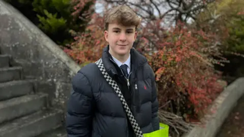 Harry es un apuesto adolescente con un peinado moderno, que lleva un sostén negro, un chaleco negro y una camisa escolar atado debajo. Estaba parado afuera de una propiedad cargando su gran bolsa de papel amarilla.