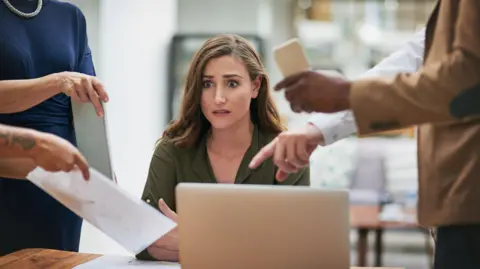 Getty Images Foto de una joven mujer de negocios que parece ansiosa en un entorno de oficina exigente.
